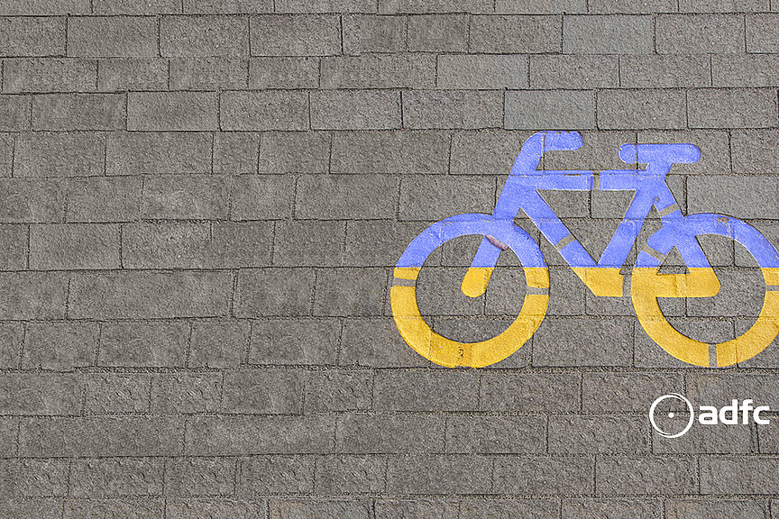 Solidaritätsbekundung Ukraine Grafik eines Fahrrads in blau-gelb auf Asphaltboden
